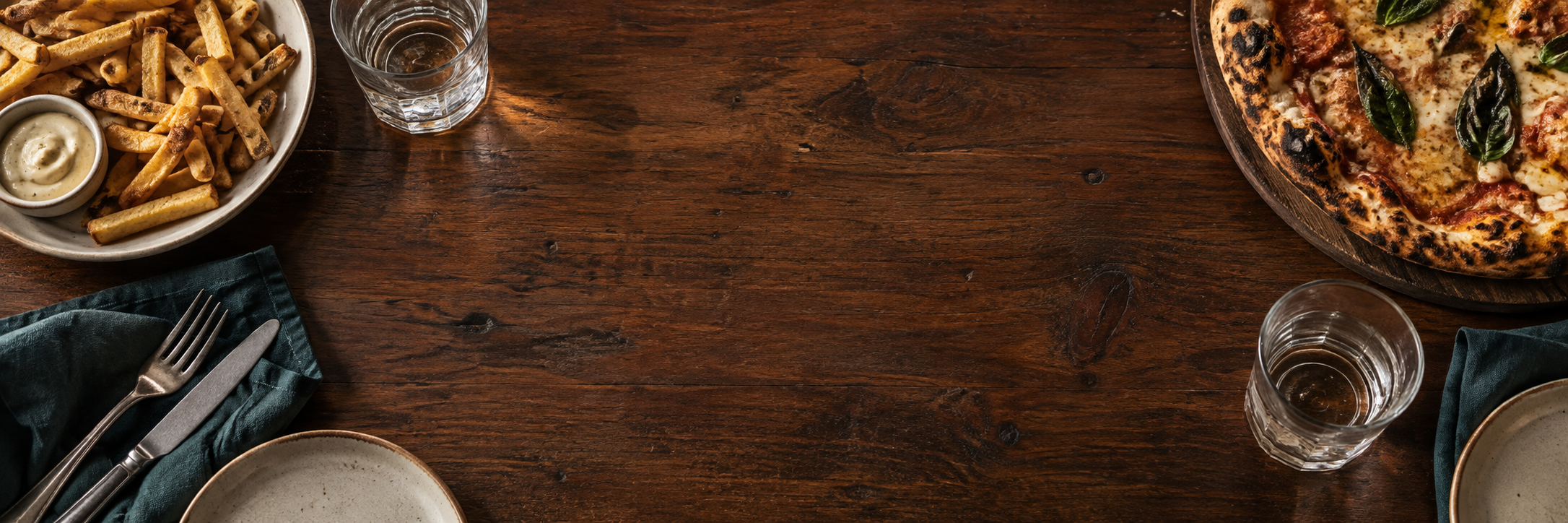 Mesa de madera con pizza, papas para compartir, vasos y servilletas turquesa